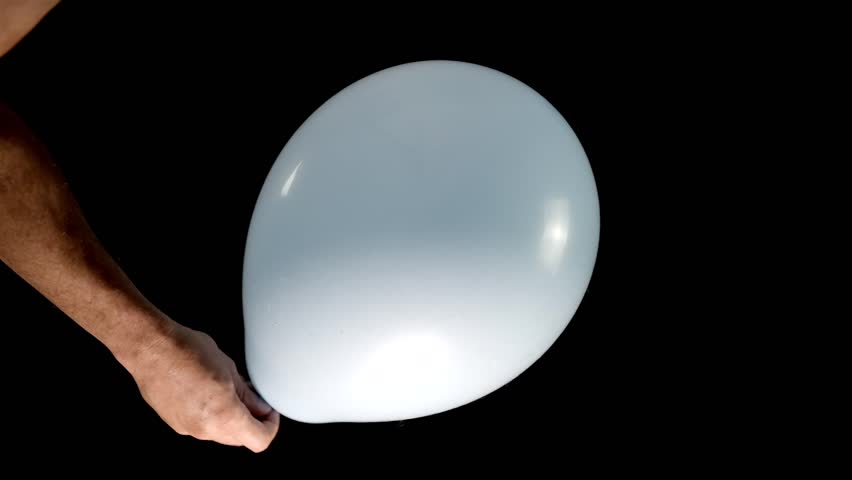 A white hand gently holds a light blue balloon and pops it with scissors. A playful and dynamic moment perfect for creative and action-filled projects. Slow motion.