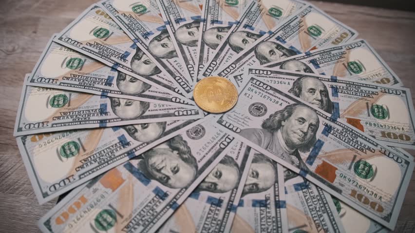 A gold bitcoin coin is centered on a fan of one hundred dollar bills, symbolizing the convergence of digital and traditional currency. Ideal for financial and tech projects.