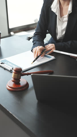 Two female lawyers in business suits meet at wooden desk, shaking hands over contract paper. wooden gavel and scales justice as discuss legal compliance, corporate law, dispute resolution.