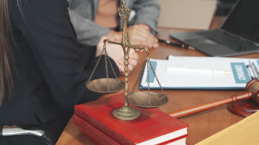 Two female lawyers in business suits meet at wooden desk, shaking hands over contract paper. wooden gavel and scales justice as discuss legal compliance, corporate law, dispute resolution.
