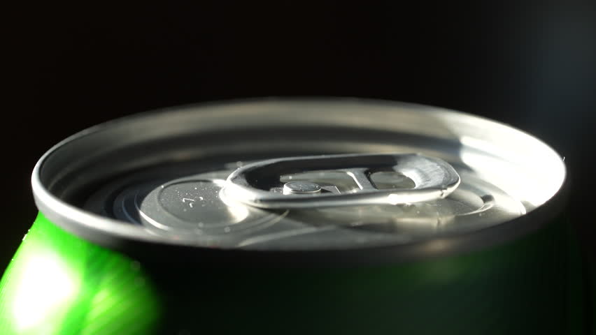 Opening metal beer can with foam, close up. Hand open a can of beer, black background