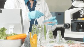 Middle-aged female laboratory worker wearing blue gloves conducts lab test on food ingredients lettuce, cucumber, pork. Using microscope, she analyzes nutrients, preservatives, food safety records. - Powered by Shutterstock - Get 15% off with code: PIKWIZARD15