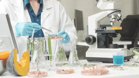 Middle-aged female laboratory worker wearing blue gloves conducts lab test on food ingredients lettuce, cucumber, pork. Using microscope, she analyzes nutrients, preservatives, food safety records. - Powered by Shutterstock - Get 15% off with code: PIKWIZARD15