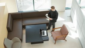 Elevated view of young standing businessman looking at financial documents while drinking coffee in office in the morning - Powered by Shutterstock - Get 15% off with code: PIKWIZARD15