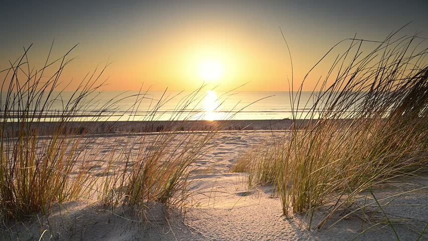 Sunset at the North Sea beach during a calm day in South Holland with gentle waves hitting the sandy beach in The Netherlands.