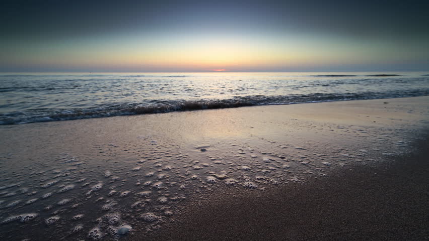 Sunset at the North Sea beach during a calm day in South Holland with gentle waves hitting the sandy beach in The Netherlands.