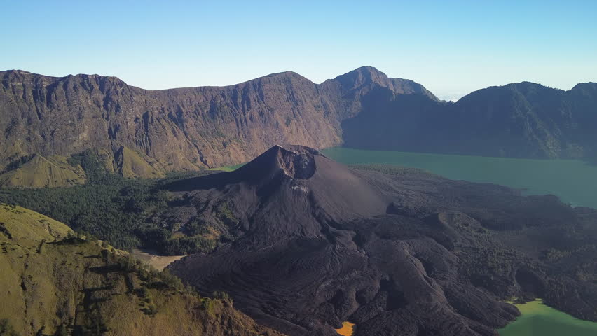 Mount Rinjani top, aerial view of Mount Barujari’s volcanic cone with dark hardened lava in Segara Anak Crater Lake on a sunny late afternoon, drone, Lombok, West Nusa Tenggara, Indonesia