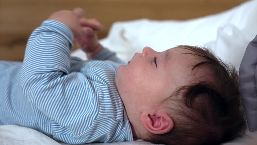 Baby lying on soft bed holding teething ring with hedgehog design, gazing upward with curiosity, gripping toy firmly, engaging in sensory play and early motor skill development