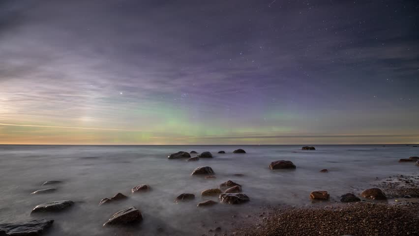 Timelapse. Scenic seashore with a boulders under a starry sky with the northern lights at dawn.