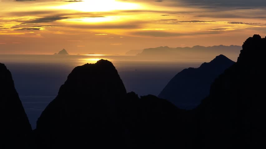 A drone view of orange sunset on silhouetted coastal mountains on Senja island in Senja Municipality in Troms County, Norway in northern Europe
