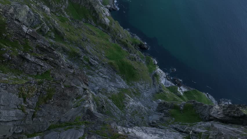 A drone view of Caucasian man standing on rocky mountaintop of Ryten-Kvalvika Beach Trail overlooking Lofoten Archipelago in Norway