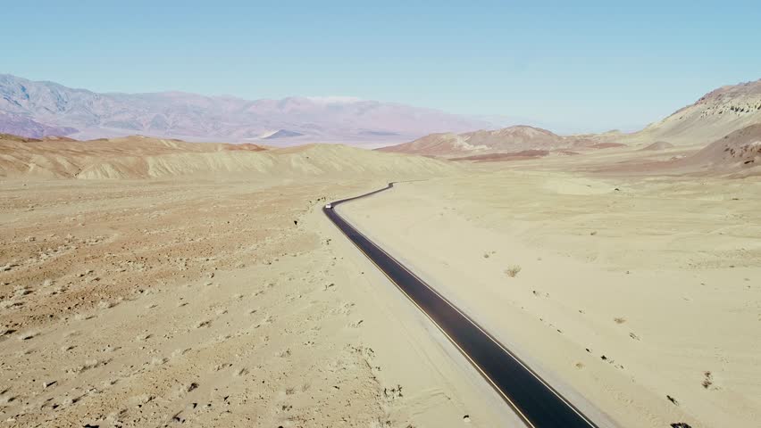 A lone white car moves along black asphalt road, Death Valley desert, clear sky