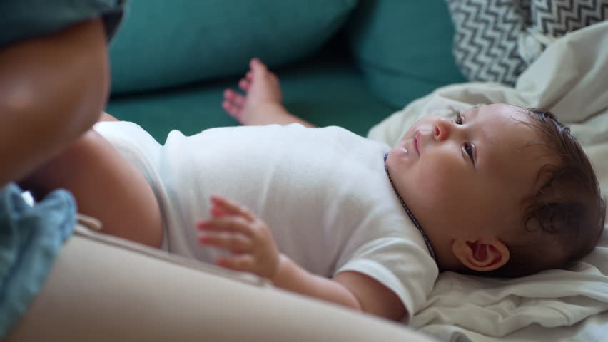 Baby lying on soft blanket, relaxed expression, gazing at parent’s hand, gentle movement, early development, warm family connection, peaceful moment at home