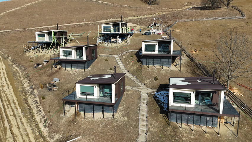 Modern hillside cabins with large glass windows, offering panoramic views of the valley, under construction in a remote countryside setting, blending nature with contemporary design