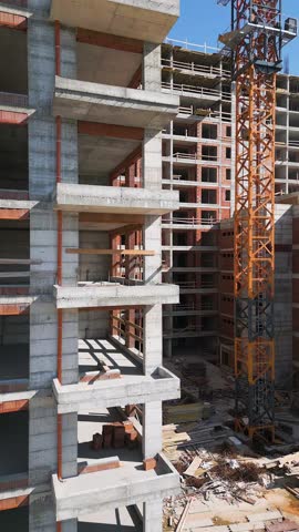 Construction site of a high-rise building at sunny day. The structure's concrete framework, cranes, and scaffolding are bathed in bright sunlight, highlighting urban development