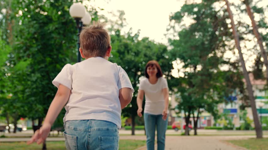 Carefree child joyful embrace of of mother. Kid has fun in summer on street with mother. Happy family Kid mom. Child, son runs to mom, hugs her in park. Mom plays with her child spins her joyful son