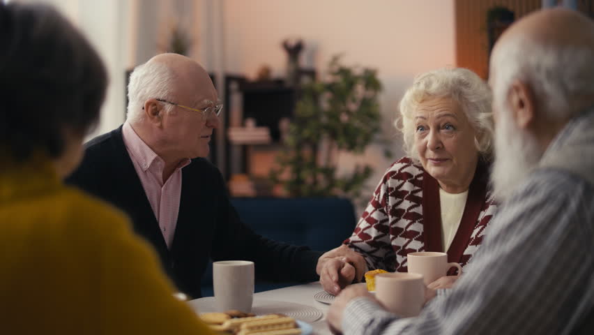 Elderly man sharing recent news with friends while drinking tea in care home