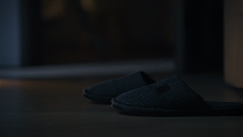 Slippers rest on a smooth floor in a cozy living room, indicating a moment of relaxation after a long day. The soft lighting enhances the calm atmosphere in the evening space
