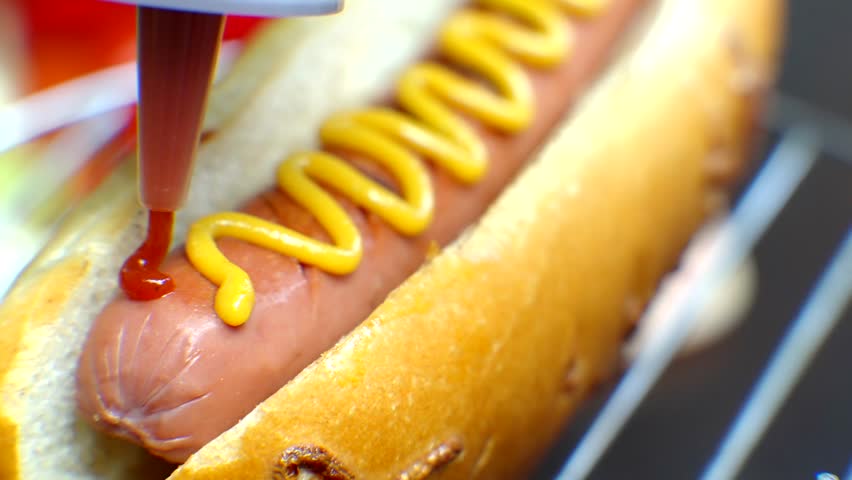 Hot Dog Served Mustard And Ketchup. American Fast Food. Tasty Hot Dog With Grilled Sausage. Appetizing Street Food. Grilled Sausage Hot dog Junk Food. Adding Ketchup And Mustard To Tasty Hot Dog Meat