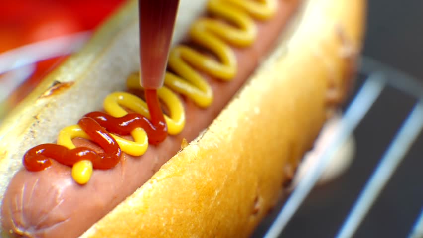 Hot Dog Served Mustard And Ketchup. American Fast Food. Tasty Hot Dog With Grilled Sausage. Appetizing Street Food. Grilled Sausage Hot dog Junk Food. Adding Ketchup And Mustard To Tasty Hot Dog Meat