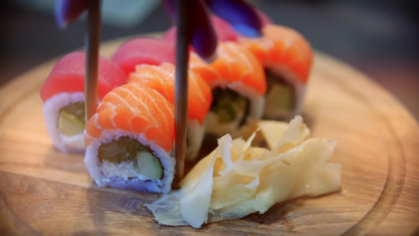 Chopsticks Take Japan Sushi In Japanese Restaurant. Traditional Sushi Maki Rolls With Salmon Philadelphia Cheese Avocado, Cucumber, Rice And Nori. Japanese Food Sushi Roll Uramaki, Nigiri And Hosomaki