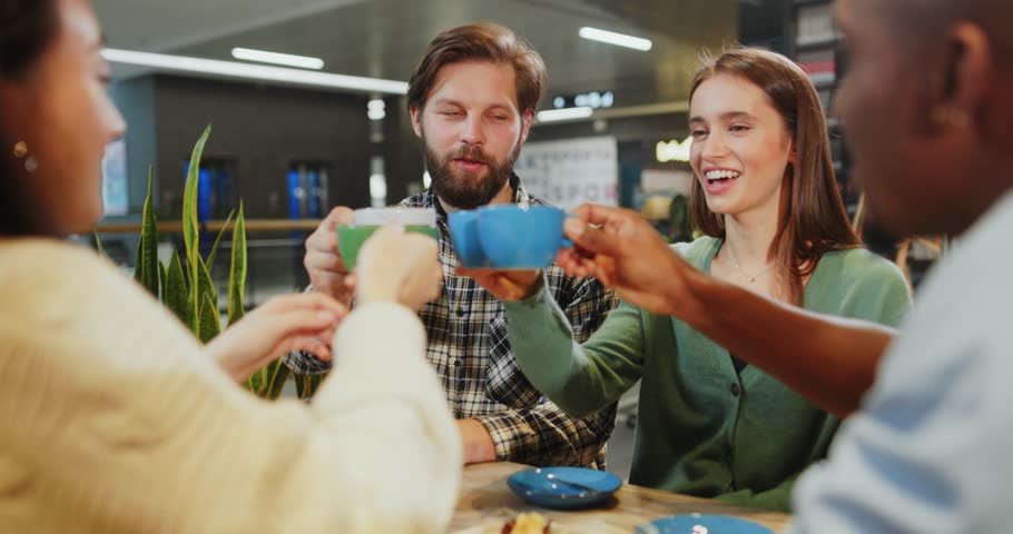 Multi-ethnic young adult friends communicating in the cafeteria sharing table enjoying their drinks and talking together. Company of best friends. Socializing.