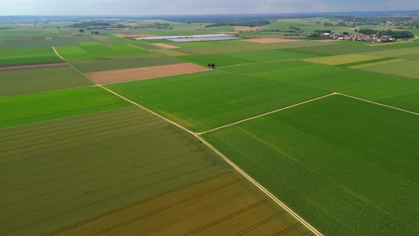 Aerial view of Bavarian farmland in Germany during summer. Green fields, dirt roads, and small chapel at crossroads. Solar panels in the background highlight sustainable farming and renewable energy. 