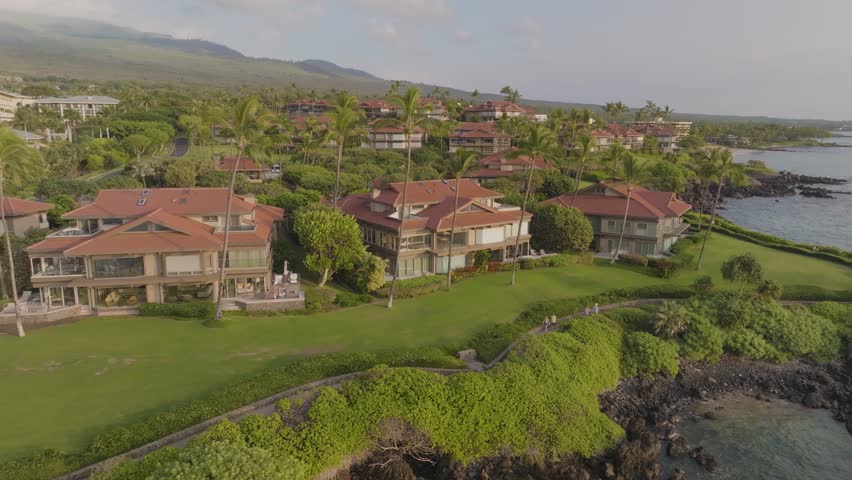 Aerial view of Wailea-Makena Maui, Hawaii oceanfront upscale villa resort and vacation homes capturing tropical landscape and seascape with people walking along beach path on shoreline - 4K Drone