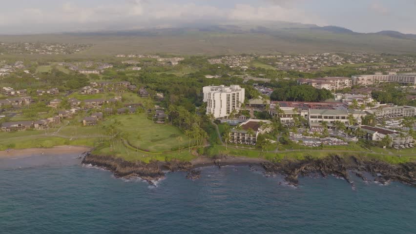 Panoramic view of Wailea-Makena Maui, Hawaii oceanfront resort hotels with tropical landscape, deep blue seascape and upscale villa vacation homes along ocean beach along volcano mountain - 4K Drone