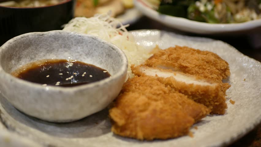 close up selective focus to a plate of crispy deep fried pork or tonkatsu, japanese food while hand using chopstick to pick up a pice of fried pork from a plate in lunch dinning restaurant time