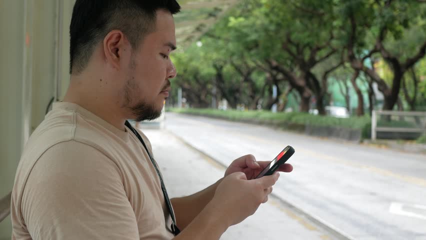 landscape view at bus stop in the city center of Taipei capital city of Taiwan while an asian man using and chatting on mobile phone waiting for upcomming bus in summer daytime.