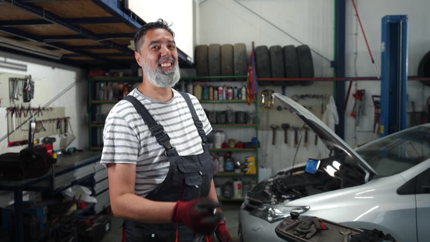 Skilled mechanic holding wrench, smiling confidently inside car repair garage during maintenance work, capturing professional expertise in slow motion