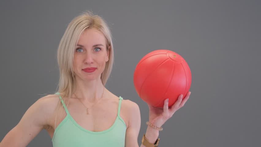 Beautiful sporty woman standing with a rubber ball on a gray background. 
