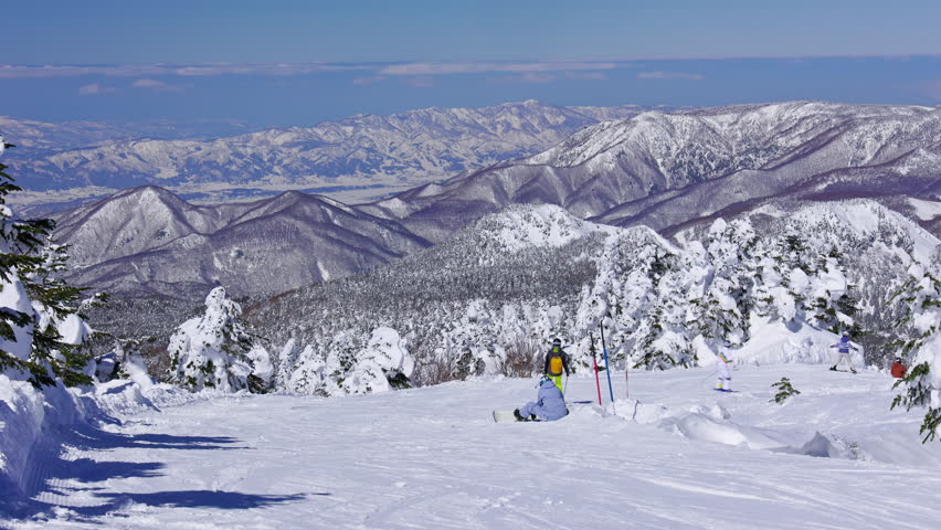 Snowboarders on a ski slope with trees and tall mountains. Yokoteyama.Handheld