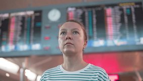 Confused woman is looking around at the airport. Departures information board is visible in background. Single traveling. Flight delay or cancellation. - Powered by Shutterstock - Get 15% off with code: PIKWIZARD15