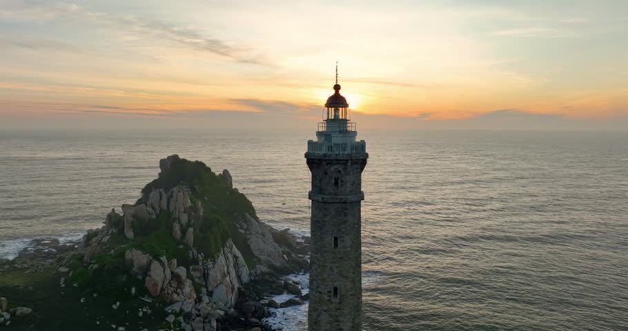 Lighthouse on the mountain peak at colorful sunset in summer. Aerial view. Beautiful lighthouse, sea and orange sky. Top view of Cape Ke Ga, Vietnam. Landscape