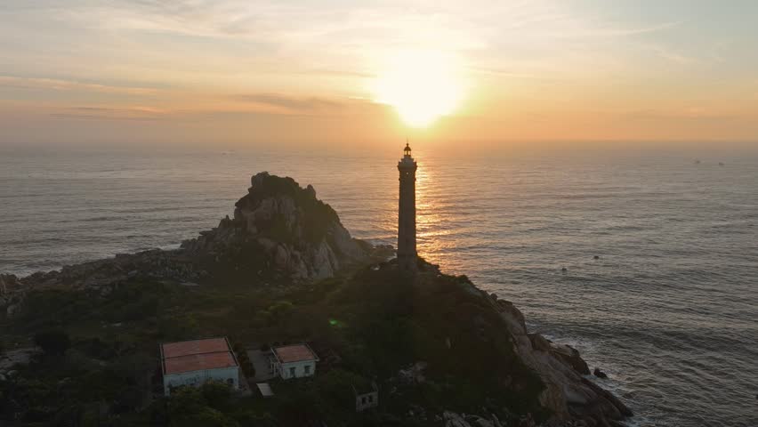 Aerial view timelapse of Lighthouse on the mountain peak at colorful sunset in summer. Aerial view. Beautiful lighthouse, sea and orange sky. Top view of Cape Ke Ga, Vietnam. Landscape