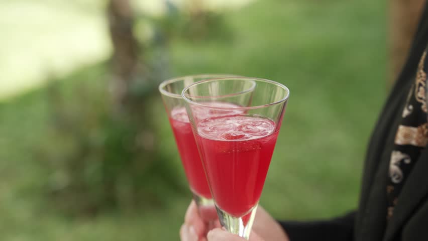 Two glasses of red cocktail held outdoors, sparkling and refreshing
