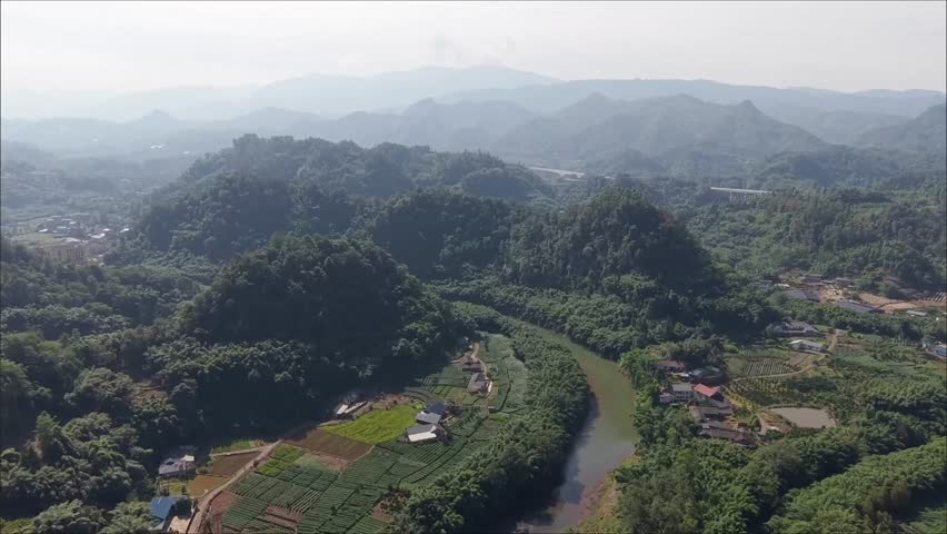 Aerial view of a lush, mountainous landscape in China. A winding river flows through verdant hills dotted with small villages and terraced fields, showcasing the serene beauty of the Chinese countrysi