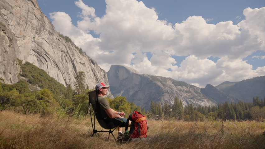 In this tranquil moment captured in Yosemite National Park, we see the stunning beauty of nature while a backpacker delights in the remarkable scenic views of their surroundings and experiences peace