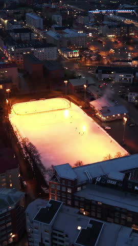 Vertical drone shot circling a illuminated ice hockey rink, dark evening in Turku
