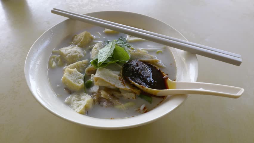 Close up of a bowl of curry mee or noodle in thick spicy gravy soup which is popular in Malaysia and Singapore. Toppings include cuttlefish, cockles, tofu and cogulated pig blood. 