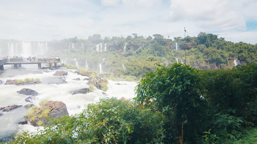 Iguazu waterfall as seen from Brazilian side. Tourists walk on the path over the river and enjoy the waterfall view