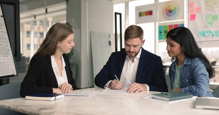 Positive young consultant woman pointing at document for business partner signing contract, explaining contract details, meeting with couple of customers in office for getting agreement