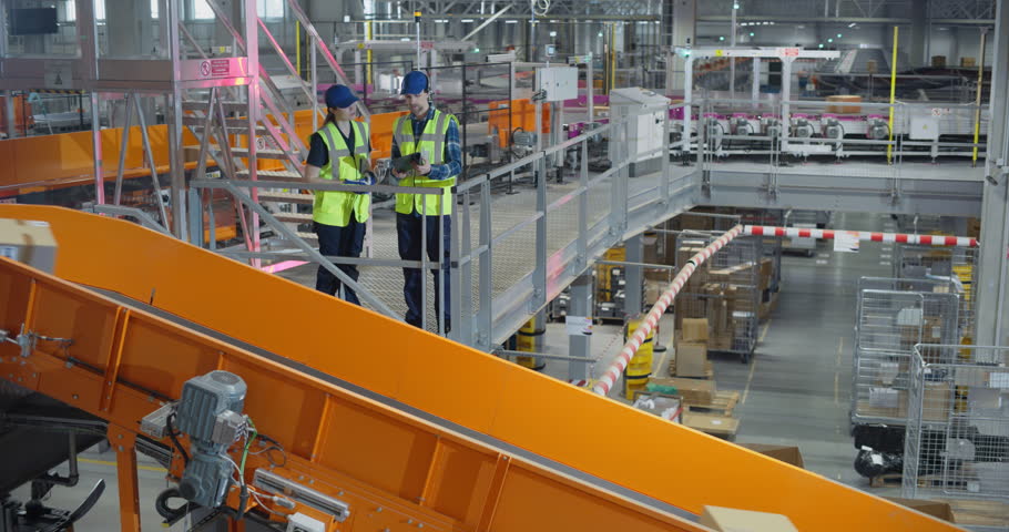 Diverse Team of Logistics Specialists Using a Tablet Computer to Oversee Parcel Sorting in a Postal Service Hub. Manager and Employee Having a Conversation while Optimizing Warehouse Productivity