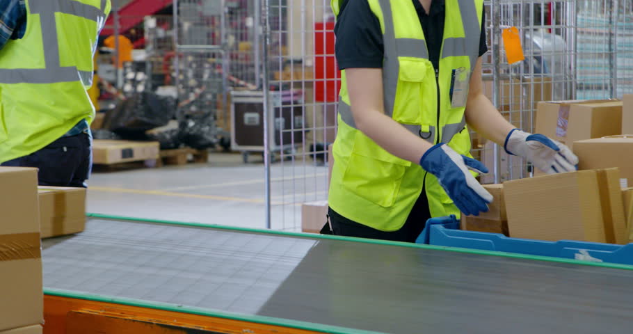 Team of Young Workers Organizing Parcels on a Conveyor in a Busy Warehouse, Ensuring Online Orders Reach Customer Delivery Without Delay. Employees in Safety Vests and Caps Handle Packages at Work