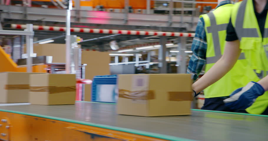 Efficient Logistics Team in Safety Vests Sorting and Loading Packages on a Conveyor Belt, Working in a Busy Distribution Center. Young Men and Female Handling Packages for Outgoing E-Commerce Orders