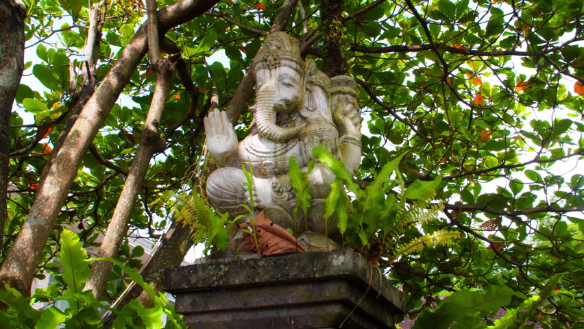 An old stone statue of Ganesha covered with moss, standing on the street