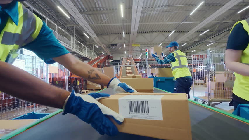 Workers in High-Visibility Vests Place a Package with a POV Camera Along a System of Conveyor Belts in a Distribution Hub. Camera Moving in Large-Scale Retail E-Commerce Logistics Service