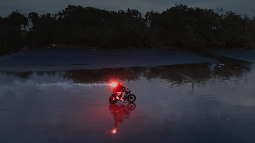 Couple riding a motorcycle on black sand beach at sunset, with a red signal flare, fire. Ocean waves and tropical scenery, romantic vibe. Man, woman driving moto bike on coastline of Bali. Road trip